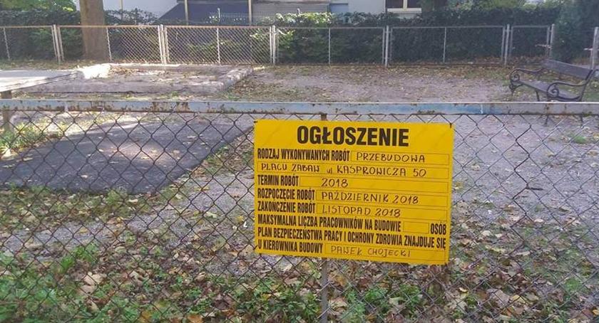 Na głównym zdjęciu znajduje się tablica informacyjna. To ogłoszenie, które pokazuje wiadomość na temat tego, kto przebuduje plac zabaw. W tle stoi budynek, na pierwszym planie ogrodzenie. 